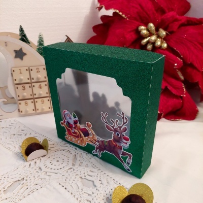 Embalagem verde decorada com Papai Noel e rena, com calendário de advento e flor vermelha no fundo