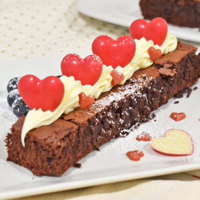 Fatia de bolo de chocolate com decoração de creme branco e corações vermelhos sobre prato branco