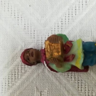 Pequena figura decorativa colorida com um cesto dourado sobre fundo branco texturizado