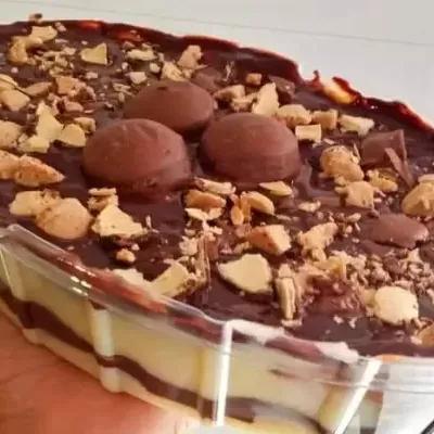 Sobremesa em tigela transparente com camadas de creme e chocolate coberta por pedaços de bolacha e bombons