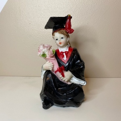 Figurina de criança em traje de graduação segurando flores e diploma