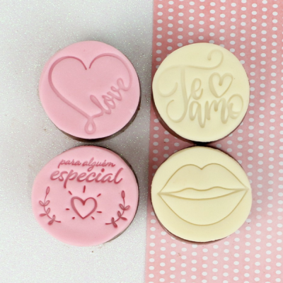 Quatro biscoitos decorados com mensagens de amor em rosa e creme