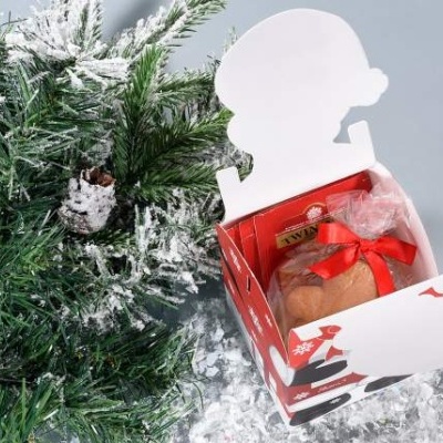 Caixa de presente natalícia aberta com pão embrulhado e ramos verdes com neve artificial