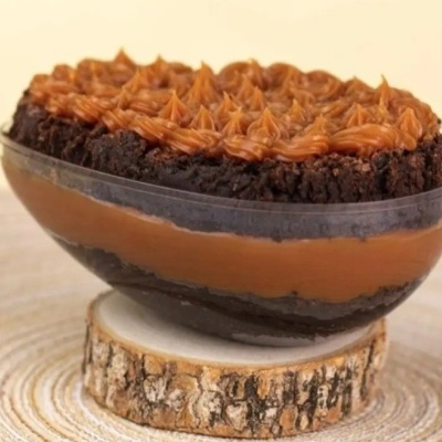 Doce com camadas de creme marrom e bolo escuro em recipiente transparente sobre base de madeira