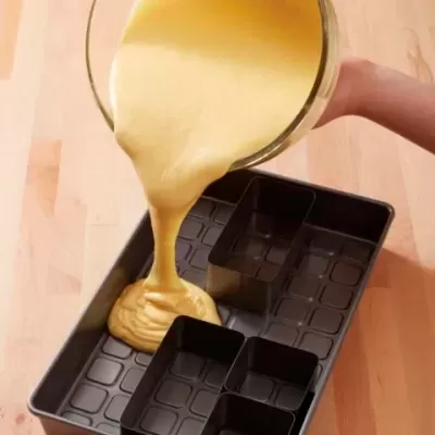 Massa amarela a ser vertida para forma de metal preta com divisórias sobre superfície de madeira clara