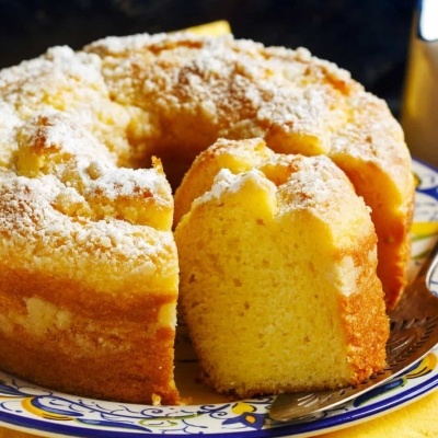 Bolo amarelo com açúcar em pó num prato colorido sobre mesa de madeira