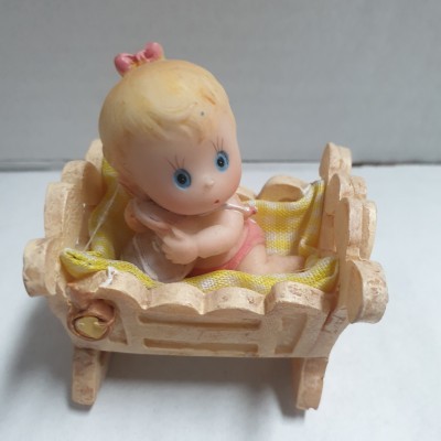 Boneca bebé cor-de-rosa numa cama de madeira clara com almofada amarela