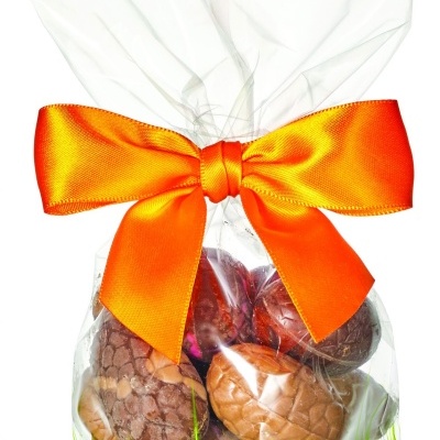 Embalagem transparente decorada com borboletas e bolas coloridas, com laço laranja e bolas de chocolate dentro.