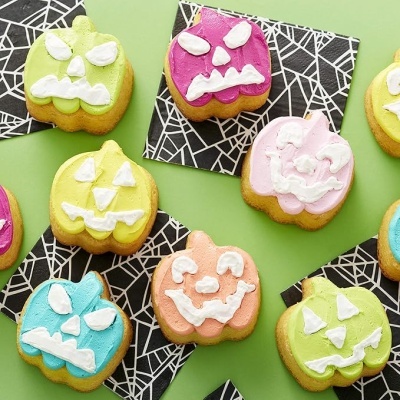 Biscoitos decorados em forma de abóboras coloridas com rostos, sobre guardanapos de teia de aranha.