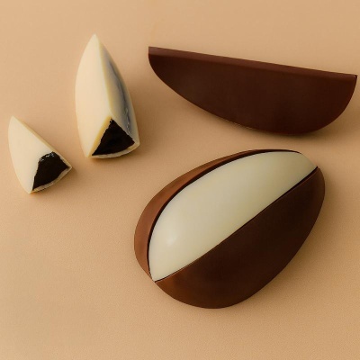 Ovos de chocolate meio amargo e branco com recheio exposto sobre fundo bege