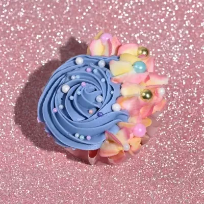 Cupcake com glacê azul, pérolas coloridas e flores artificiais sobre glitter rosa