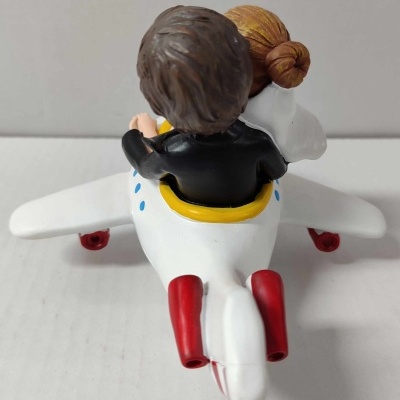 Casal sentado em avião decorativo branco com detalhes coloridos visto de costas