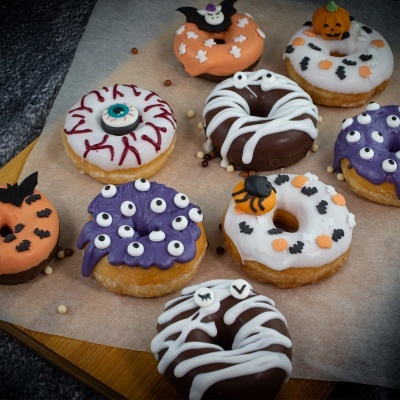 Donuts decorados de Halloween com glacê colorido e temas assustadores sobre papel vegetal numa tábua de madeira