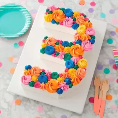 Bolo número 3 decorado com flores coloridas em mesa de festa