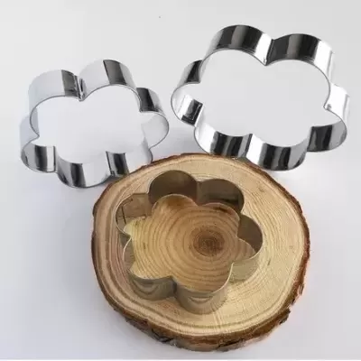 Três cortadores metálicos em forma de flor com superfície de madeira e fundo branco