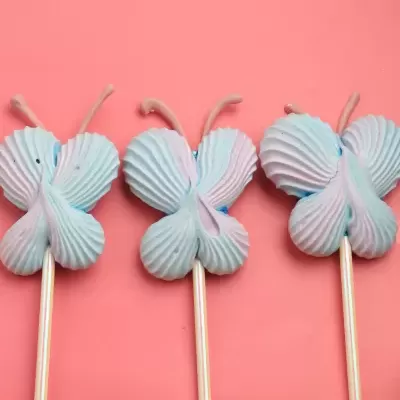 Três pirulitos em forma de borboleta azuis e rosa sobre fundo cor de rosa