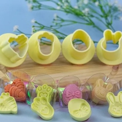 Cortadores de bolachas amarelos com formas de cenoura, pata, ovo e coelho sobre base de madeira com bolachas coloridas