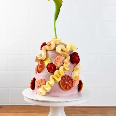 Bolo rosa decorado com frutas secas e flores em suporte branco