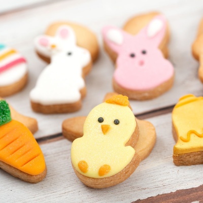 Biscoitos decorados de coelhos, cenoura e pintainho sobre mesa de madeira clara