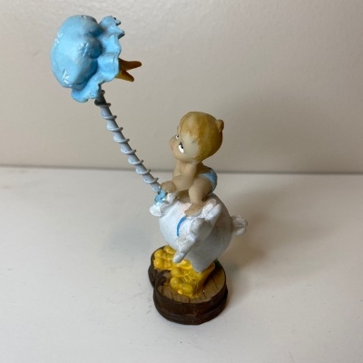 Figurine de bebé numa galinha branca com balão azul em mola