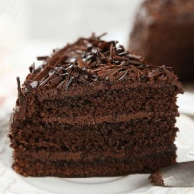Fatía de bolo de chocolate com várias camadas e raspas de chocolate num prato branco