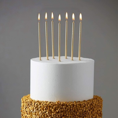 Bolo de aniversário branco com velas douradas acesas e sementes douradas na base