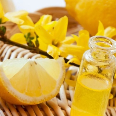 Frasco de vidro com líquido amarelo, limão cortado e flores amarelas no cesto de vime.