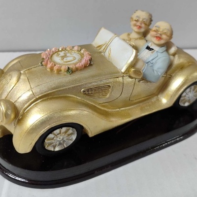 Figura de idosos num carro antigo dourado em base preta