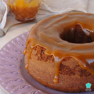 Bolo de chocolate com cobertura caramelizada num prato lilás, com colher e copo ao fundo