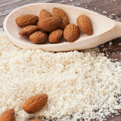 Colher de madeira com amêndoas inteiras sobre farinha de amêndoa numa mesa de madeira