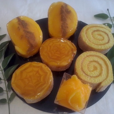 Seis doces variados em prato preto com folhas verdes ao lado