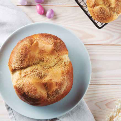 Dois pães dourados em prato e grelha, com pastilhas coloridas em tigela sobre mesa de madeira clara