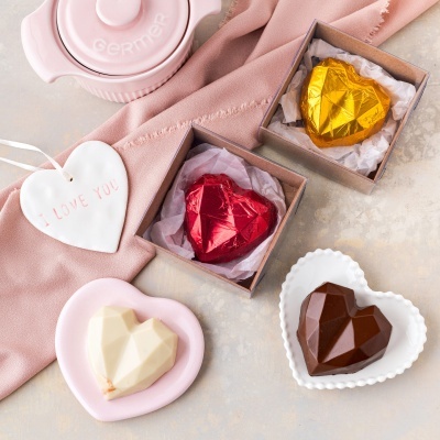 Chocolates em forma de coração em embalagens e pratos decorativos sobre pano rosa e superfície clara