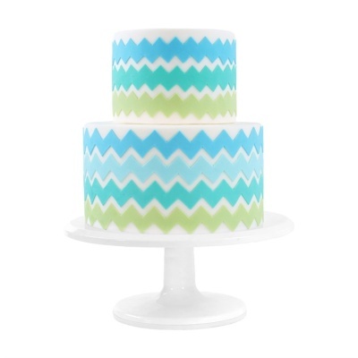 Bolo decorado em suporte branco com padrão zig-zag azul, verde e branco