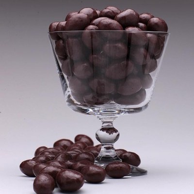 Taça de vidro com amêndoas cobertas de chocolate preto e algumas amêndoas à base.