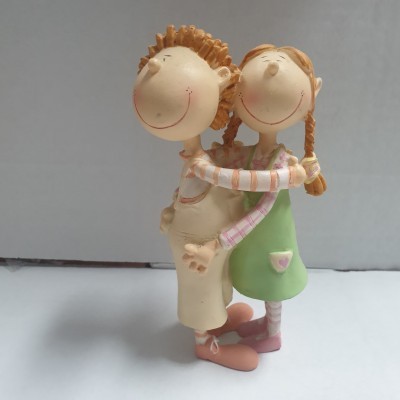 Figura decorativa de menino e menina com vestido verde e calças bege, sorridentes e de braços dados