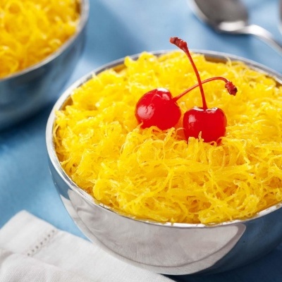 Dois recipientes metálicos com doce amarelo e cerejas em cima sobre tecido azul