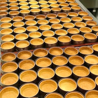 Bases de tarte douradas e uniformes em tabuleiros de produção alimentar