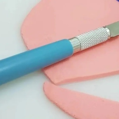 Faca de precisão com cabo azul e lâmina metálica prateada a cortar pasta rosa