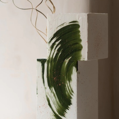 Escultura branca com pincelada verde e ramos secos em fundo bege