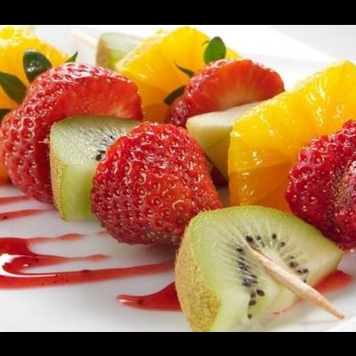 Espetadas de fruta com morangos, kiwi e laranja num prato branco com molho vermelho
