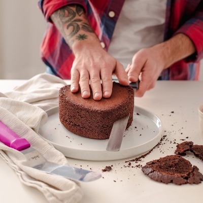 Bolo de chocolate redondo sendo cortado por pessoa com camisa xadrez