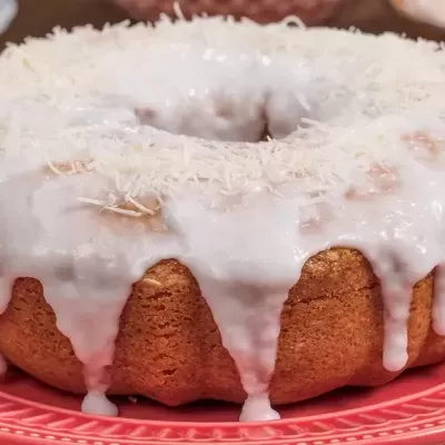 Bolo com cobertura branca escorrendo num prato vermelho com padrão.