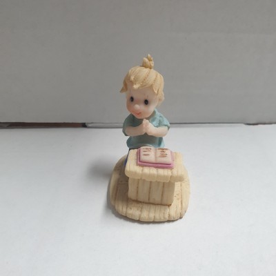 Figurina de menino ajoelhado junto a uma pequena mesa com livro aberto