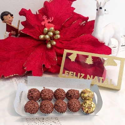 Brigadeiros em bandeja com decoração natalícia vermelha e dourada, flor e figura de rena branca