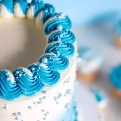 Bolo branco e azul decorado com creme e bolinhas coloridas