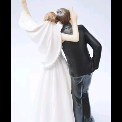 Figuras de casal em pose de abraço, mulher com vestido branco e homem com fato preto.