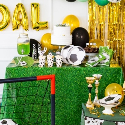 Mesa de festa decorada com tema futebol, com balões, bolo, bolas de futebol e troféus.