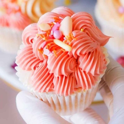 Cupcake com cobertura rosa cremosa, granulado colorido e amêndoas, segurado por mão enluvada