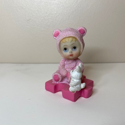 Figura de bebé com fato rosa e coelho branco numa base rosa
